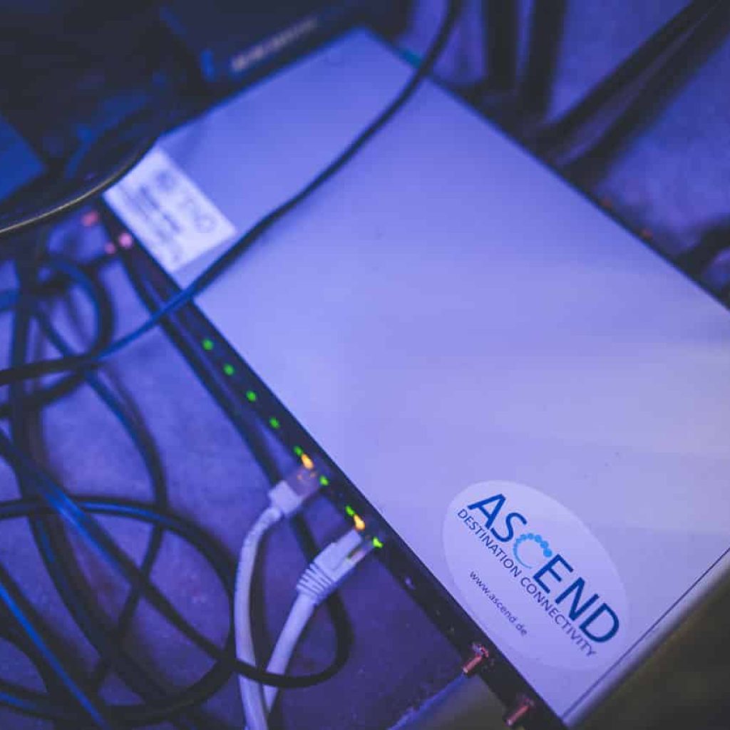 Mobile router from Peplink, model HD4, with three SIM cards inserted and connected. The device has mobile phone antennas and WiFi antennas, both of which are connected. A sticker with the ASCEND logo is clearly visible on the device.