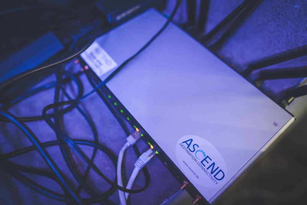 Router móvil de Peplink, modelo HD4, con tres tarjetas SIM insertadas y conectadas. El aparato tiene antenas de telefonía móvil y antenas WiFi, ambas conectadas. En el aparato se ve claramente una pegatina con el logotipo de ASCEND.
