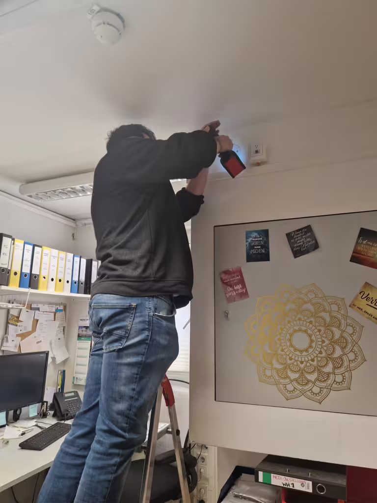 Mann auf Leiter installiert Gerät im Büro.